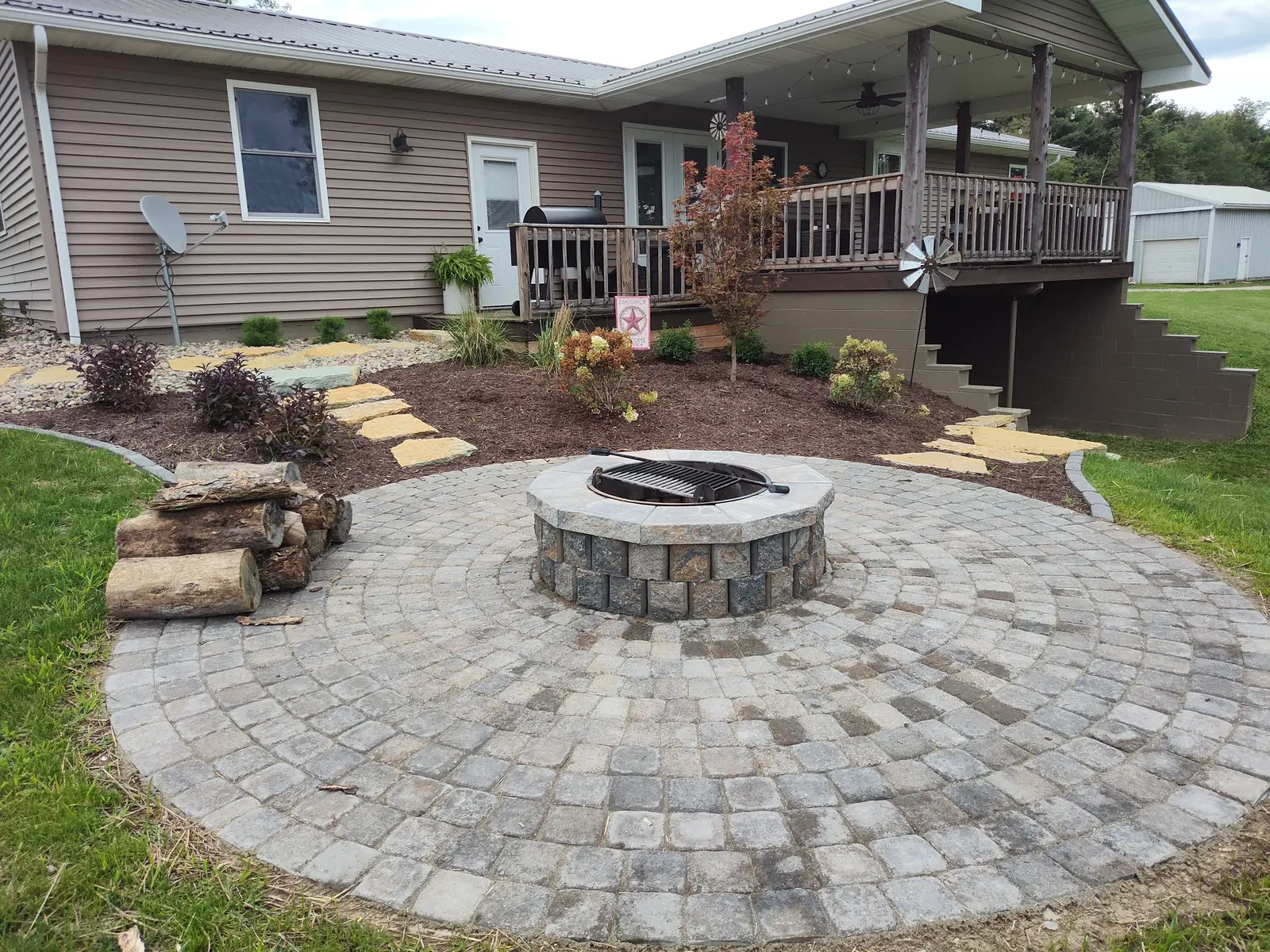 Circular paver fire pit courtyard beside a raised deck by Dave's Landscaping