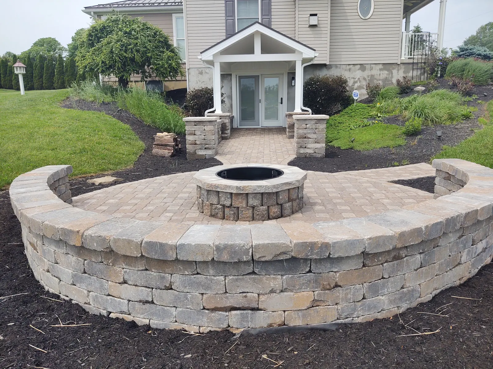 Circular fire pit patio and seat wall outside a lower-level entry by Dave's Landscaping