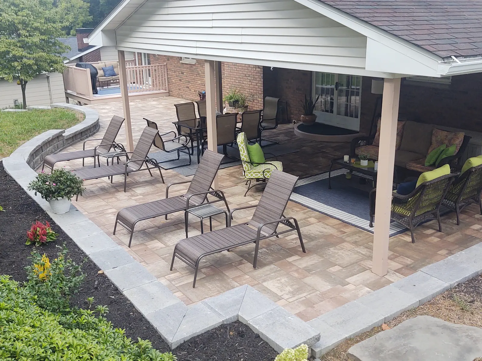Large paver patio extending from a covered porch by Dave's Landscaping