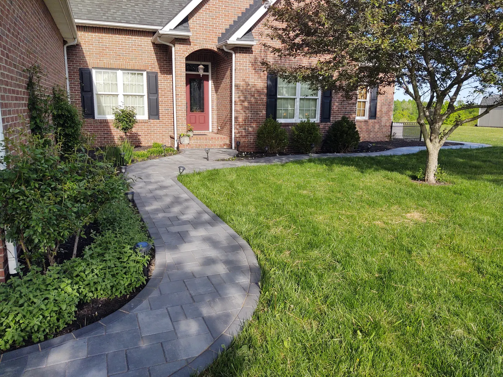 Curved paver walkway wrapping a manicured front lawn by Dave's Landscaping