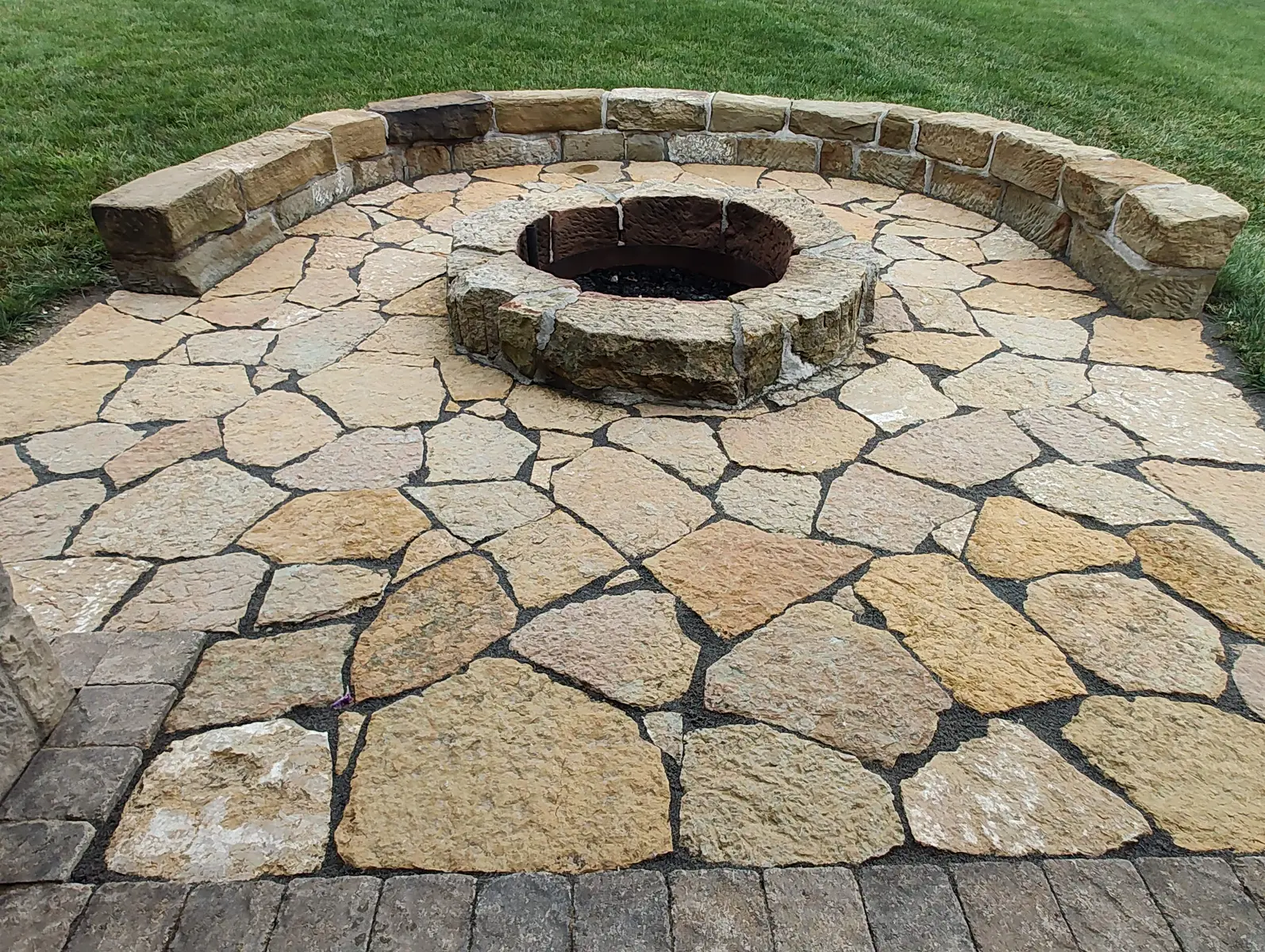 Natural flagstone patio surrounding a stone fire pit by Dave's Landscaping