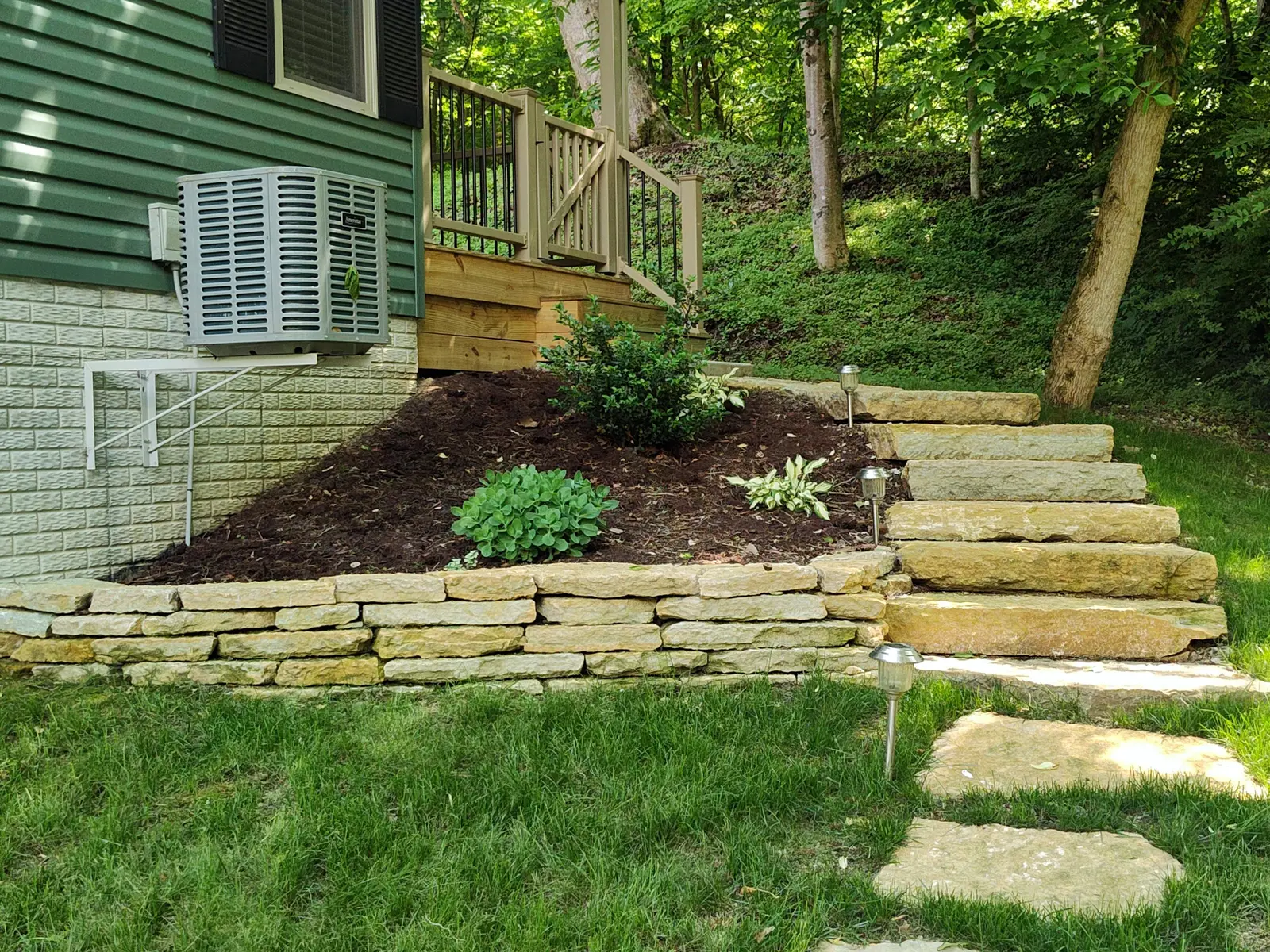 Stone retaining wall and garden steps beside a wooded home by Dave's Landscaping