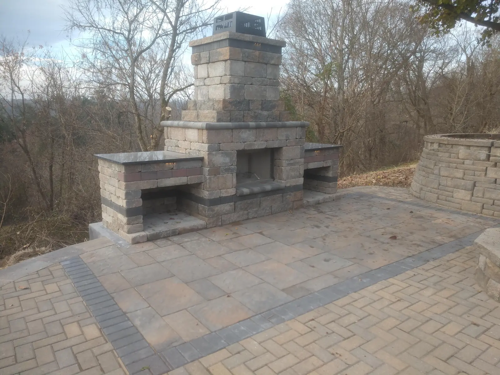 Outdoor fireplace and seat walls in a woodland setting by Dave's Landscaping