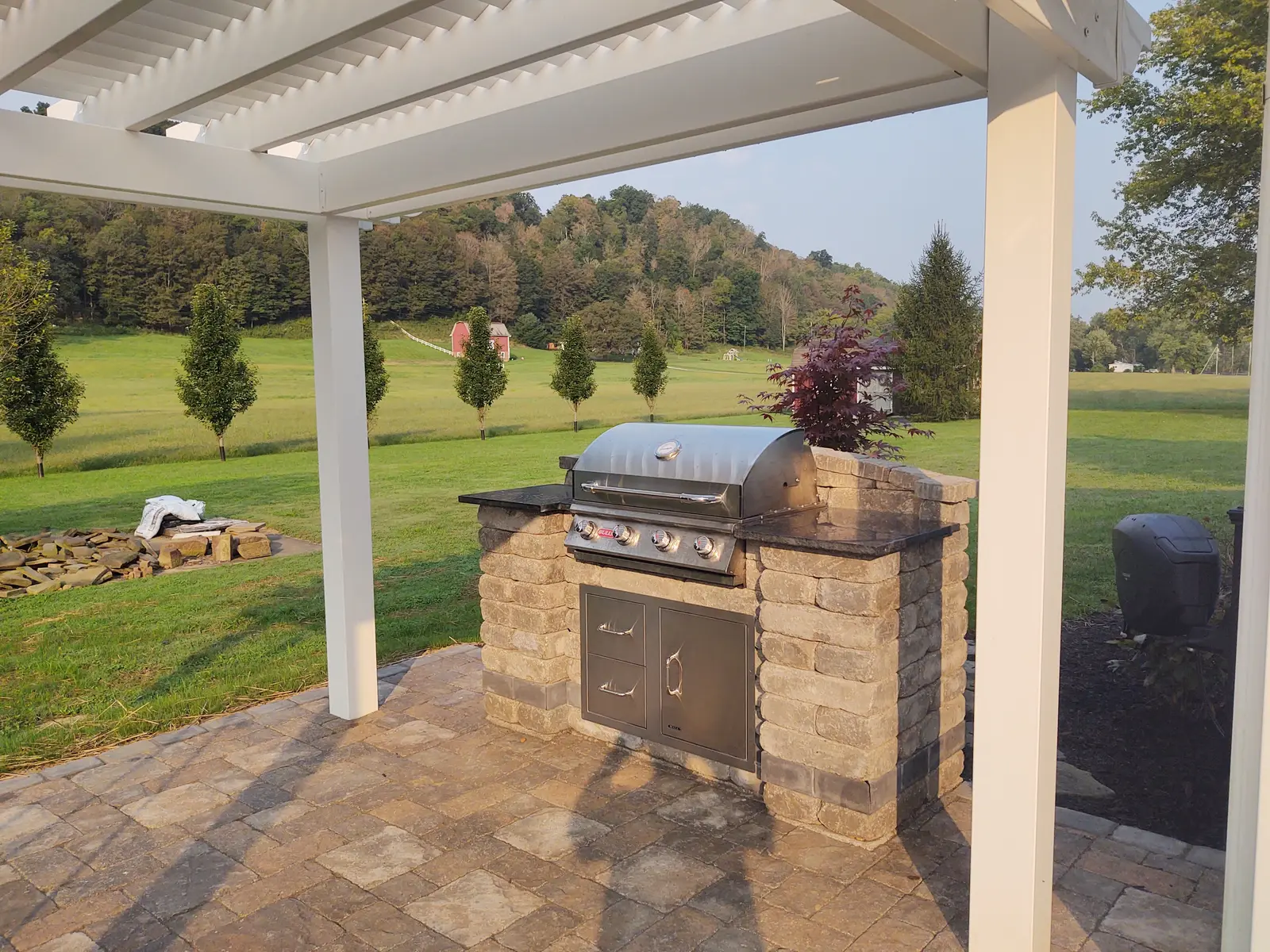 Covered grill island with stone columns and country views by Dave's Landscaping