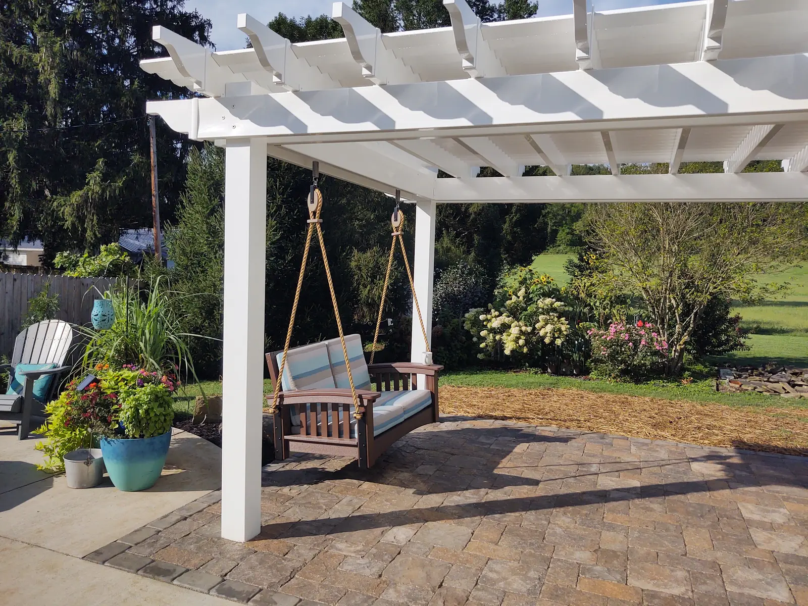 White pergola and garden swing over a paver patio by Dave's Landscaping
